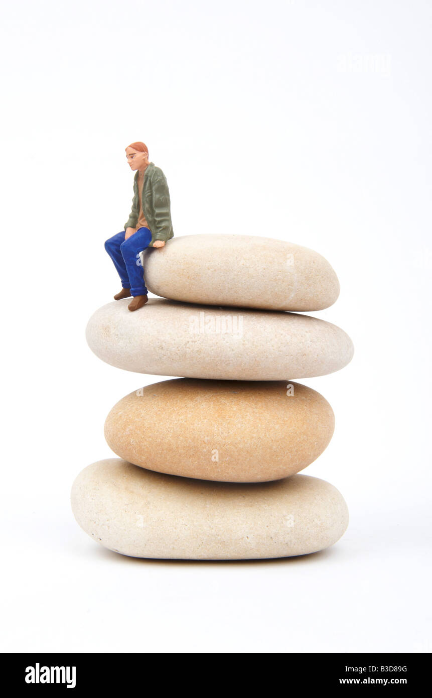 Mediation, balance, thinking, solitude, loneliness, isolation, mediation, solitude, mental health concept - figure on pile of pebbles - studio Stock Photo