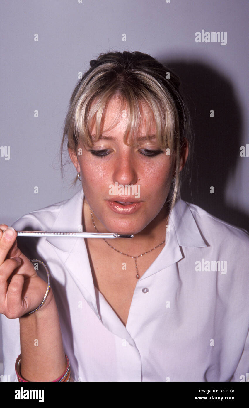 A schoolgirl blows on a thermometer to show that humans produce heat Stock Photo