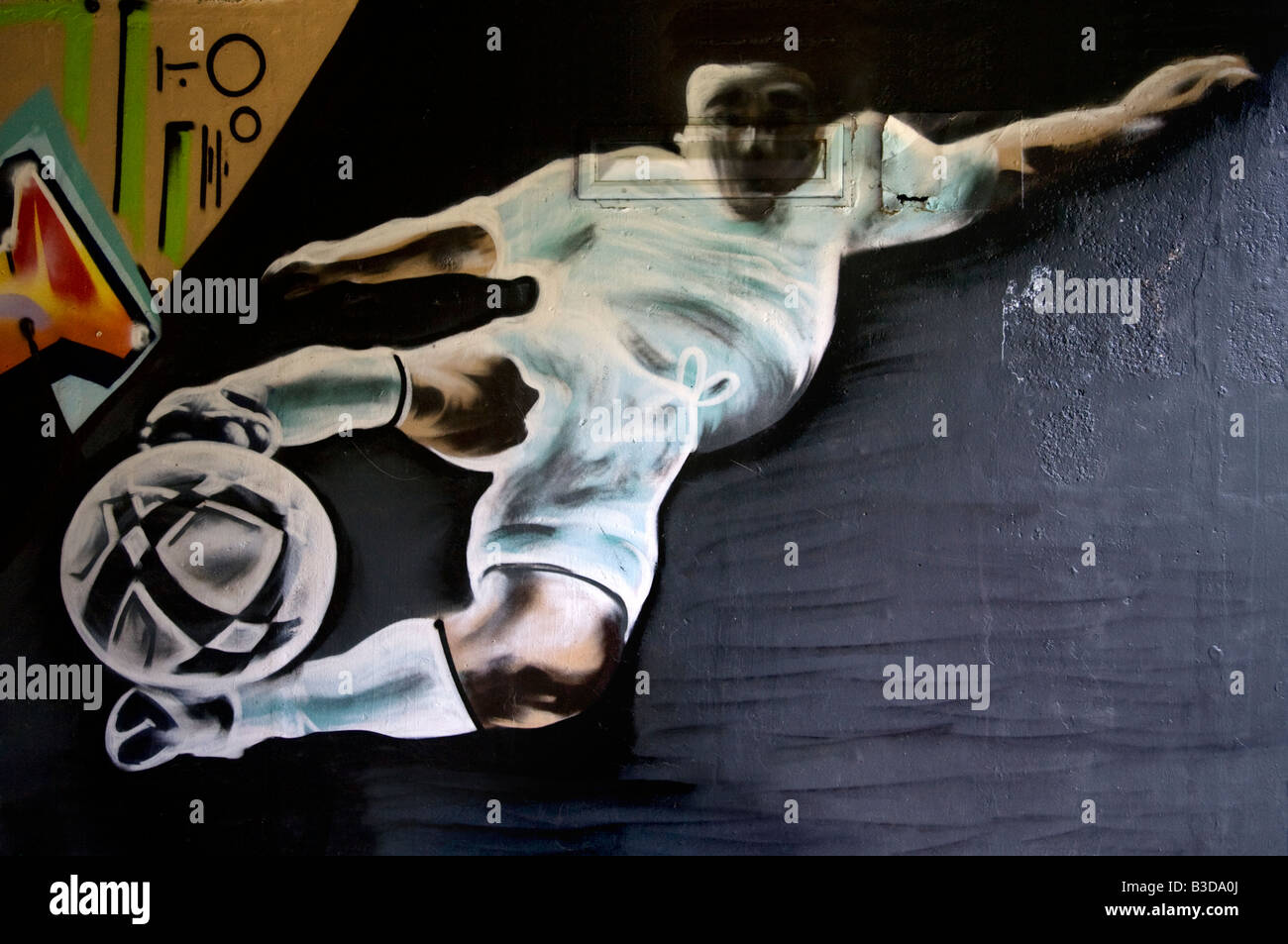 A graffiti image of a soccer player kicking a football painted on a wall. Stock Photo