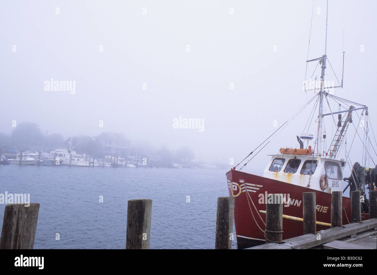 Red fishing boat tied to pier in harbor in fog at Falmouth Harbor, Cape Cod, USA. Stock Photo