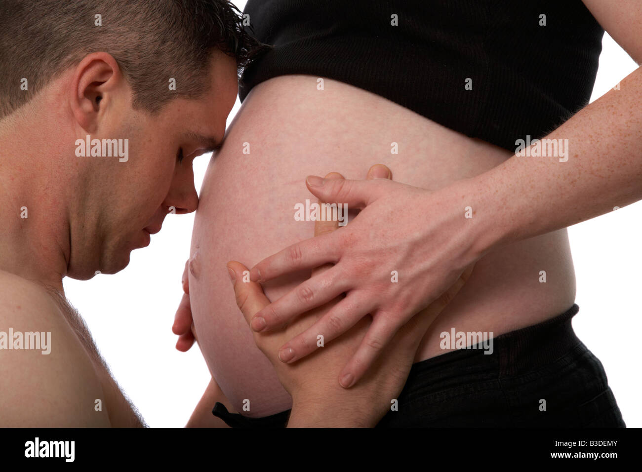 8 month pregnant mid twenties woman 25 years of age with 25 year old male partner caressing the baby bump belly Stock Photo