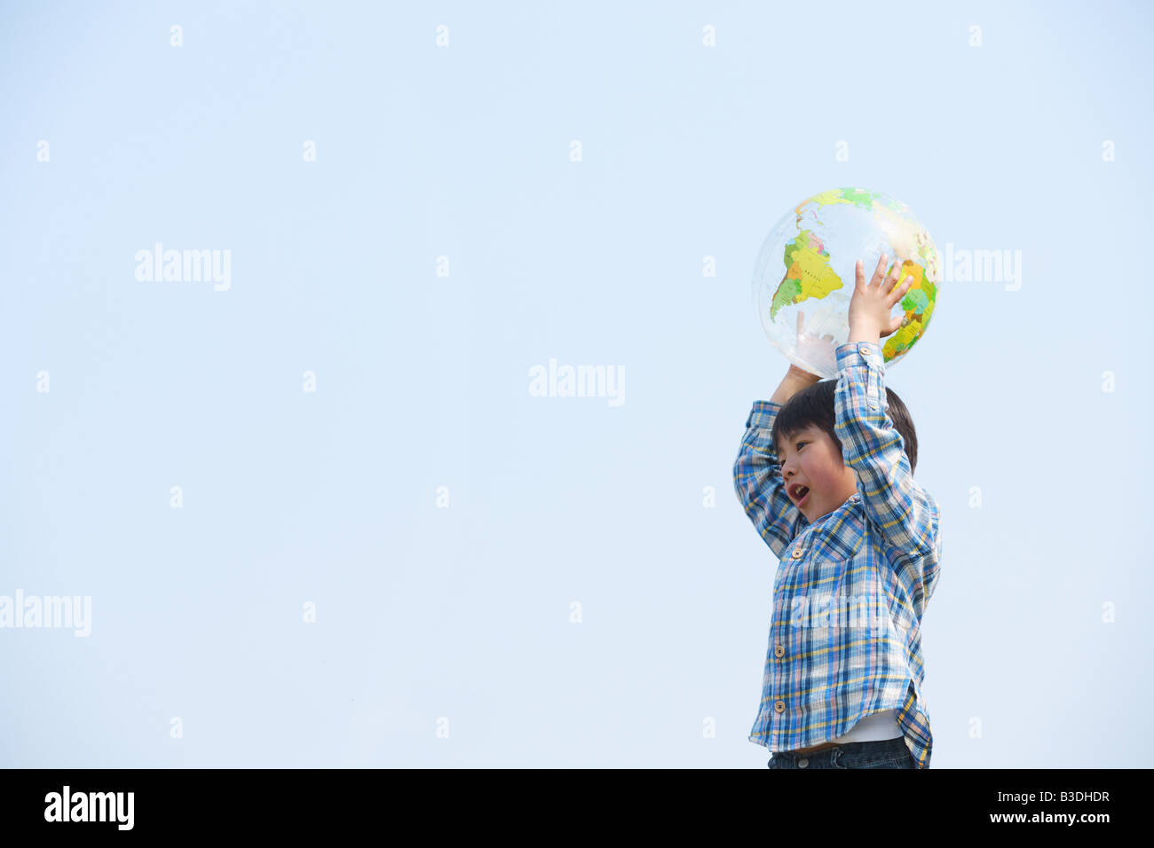 Boy playing with ball against blue sky Stock Photo