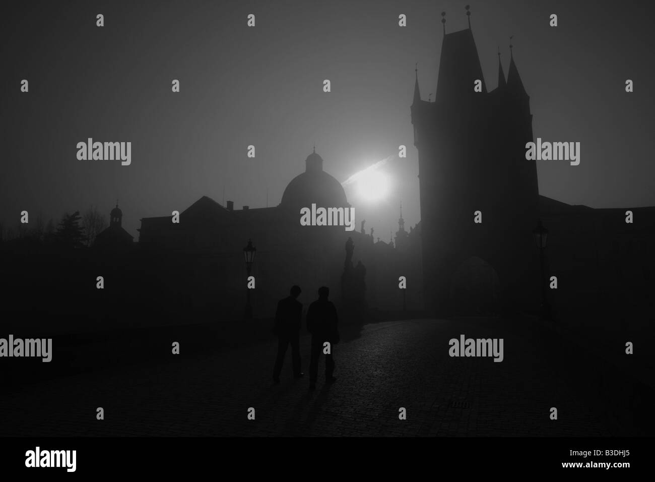 Pedestrians walk across the historic Charles Bridge, Prague with rows of Baroque statues blanketed in fog Stock Photo