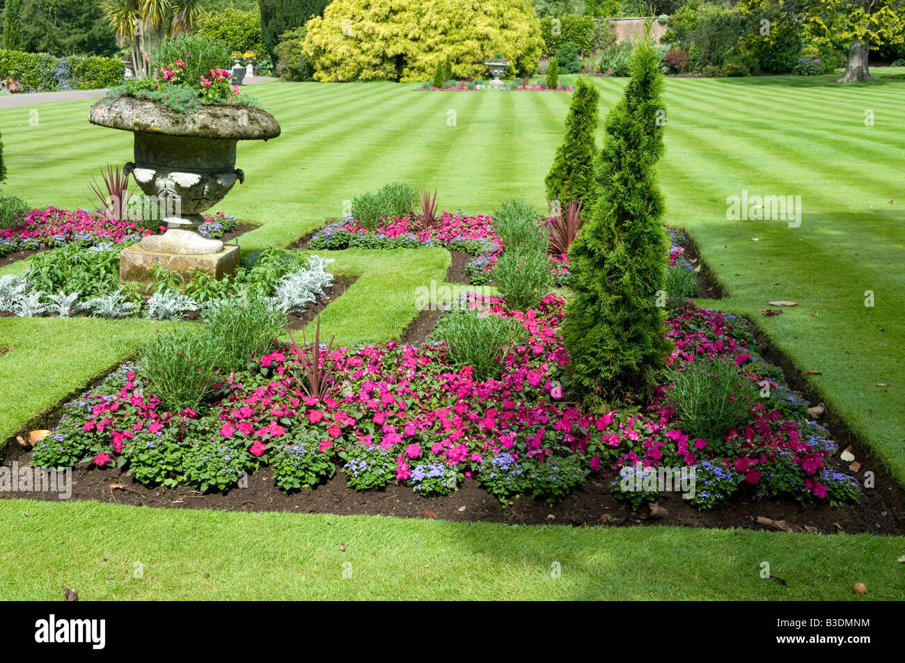 Shaped flower bed with stone vessel centre piece & dwarf conifers. Stock Photo