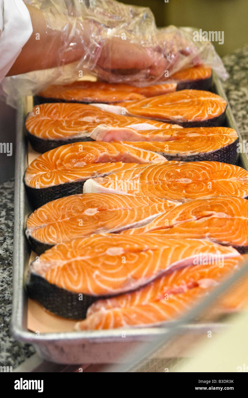 Vendor wearing gloves prepares a tray of farmed Atlantic salmon steaks for sale Stock Photo