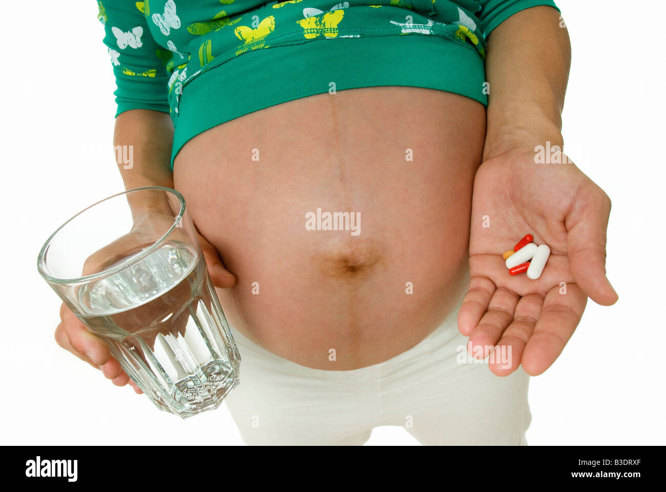 PREGNANT WOMAN HOLDING VITAMIN PILLS AND GLASS OF WATER Stock Photo