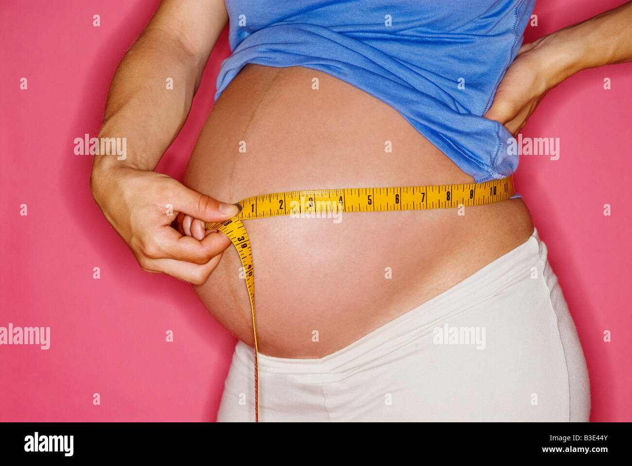 PREGNANT WOMAN MEASURING HER ABDOMEN WITH A MEASURING TAPE. PREGNANCY Stock Photo