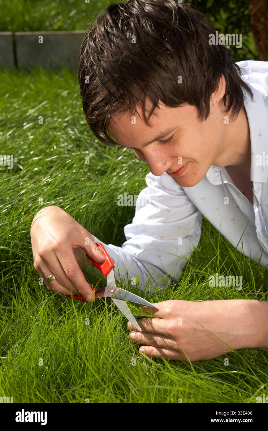 young dark haired man late teens early twenties cutting grass in a garden with a pair of scissors Stock Photo