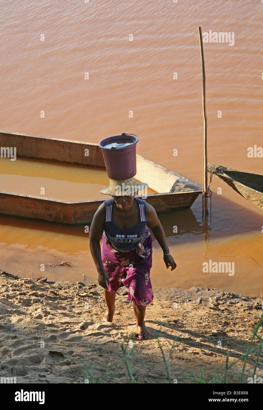 woman is carrying a bucket on her head up a bank slope Frau trägt Wassereimer auf dem Kopf eine Uferböschung hinauf Stock Photo