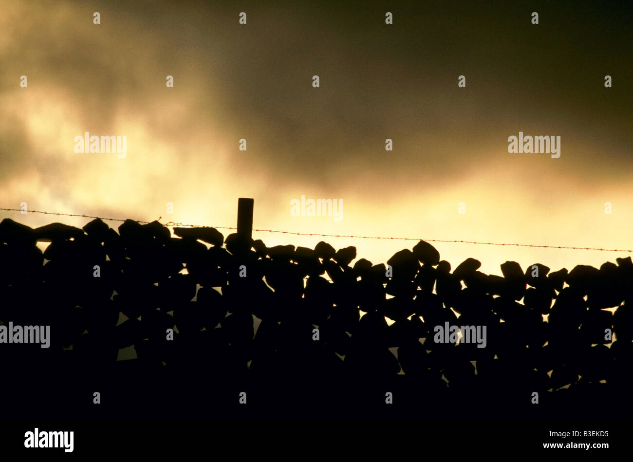 RURAL NORTHERN IRELAND DARK MISTY CLOUDS SET AGAINST HAZY YELLOW SUNLIGHT OVER SILHOUETTE OF DRY STONE WALL CO ANTRIM 1992 Stock Photo