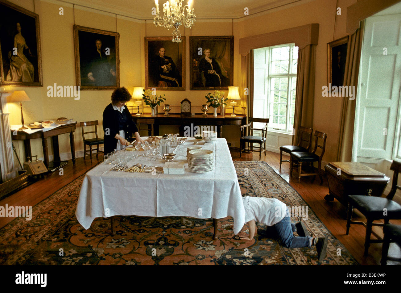 A boy hiding underneath the dinner table in the dining room of a stately mansion Stock Photo