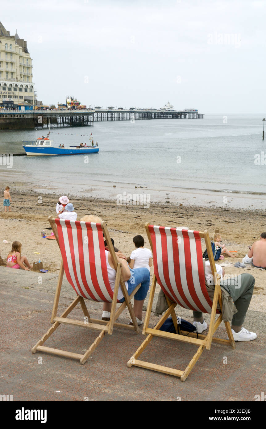 A couple sat in deckchairs overlooking Llandundo beach and pier Stock Photo