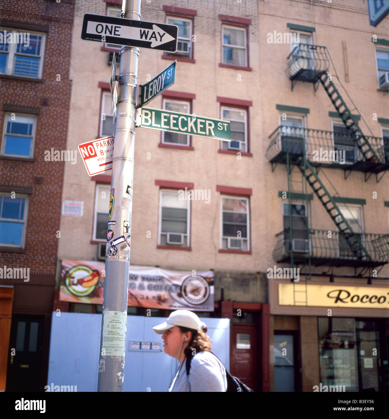 A young woman waiting on Leroy and Bleecker Street under a street sign and a signpost in Greenwich Village, NYC June 2008 Stock Photo