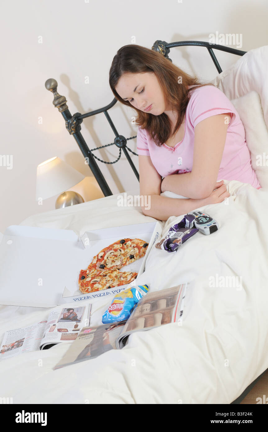 a girl in bed eating junkfood feeling ill and sick Stock Photo Alamy