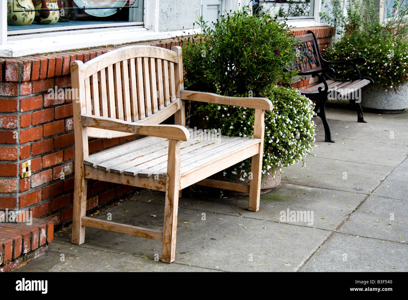 Wooden bench in front of a brick wall by a sidewalk next to a bush in ...