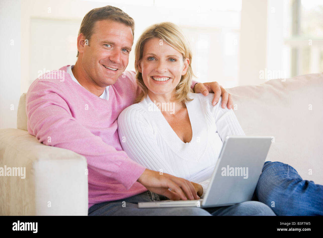 Couple in living room using laptop and smiling Stock Photo - Alamy