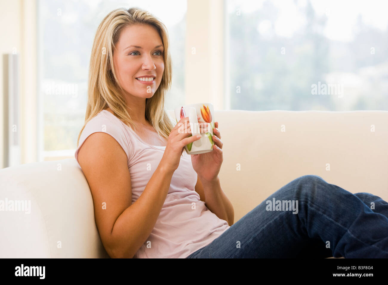 Woman in living room with coffee smiling Stock Photo - Alamy