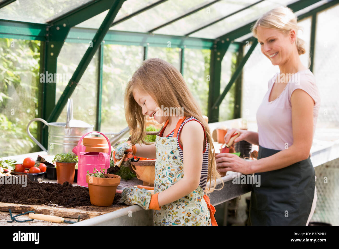 Young girl and woman in greenhouse putting soil in pots smiling Stock ...
