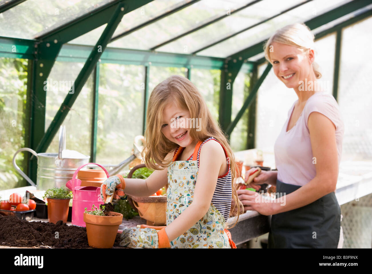 Young girl and woman in greenhouse putting soil in pots smiling Stock ...