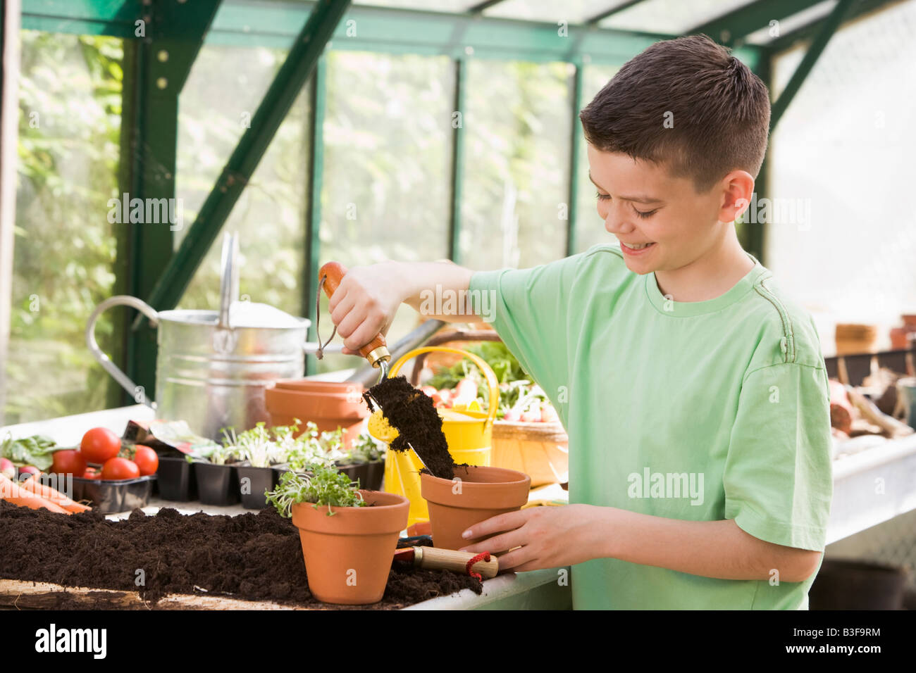 Young boy in greenhouse putting soil in pot smiling Stock Photo - Alamy