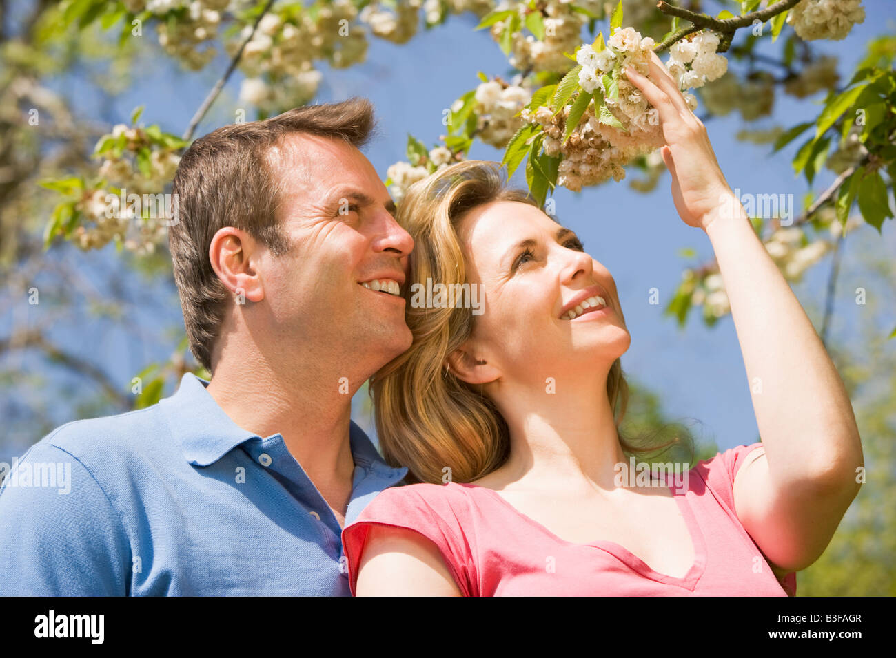 Couple standing outdoors holding blossom smiling Stock Photo - Alamy