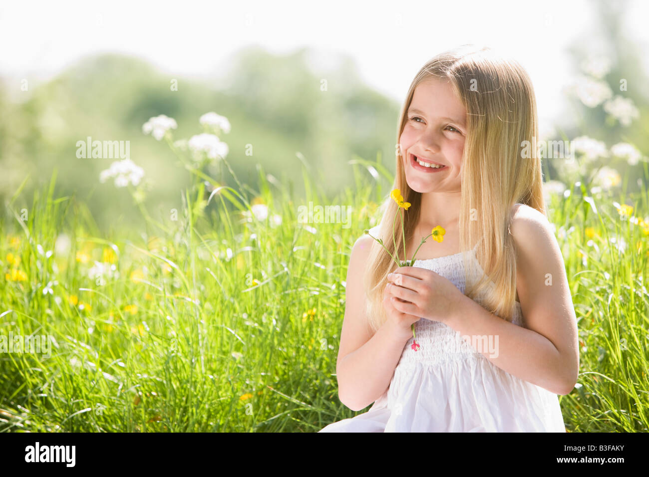 Young girl sitting outdoors holding flower smiling Stock Photo - Alamy