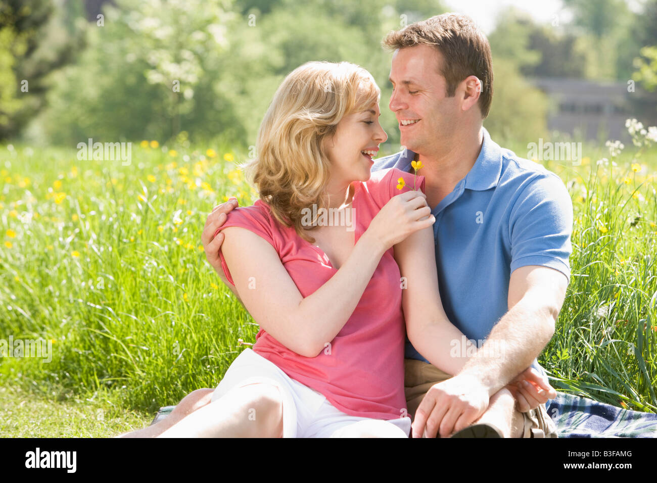 Couple sitting outdoors holding flower smiling Stock Photo - Alamy