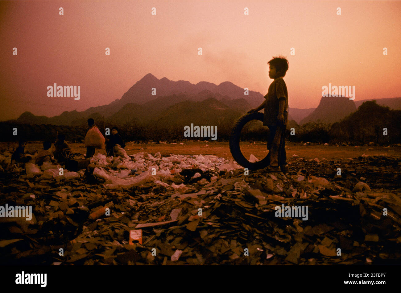 child holding tyre standing amidst a landfill site Stock Photo