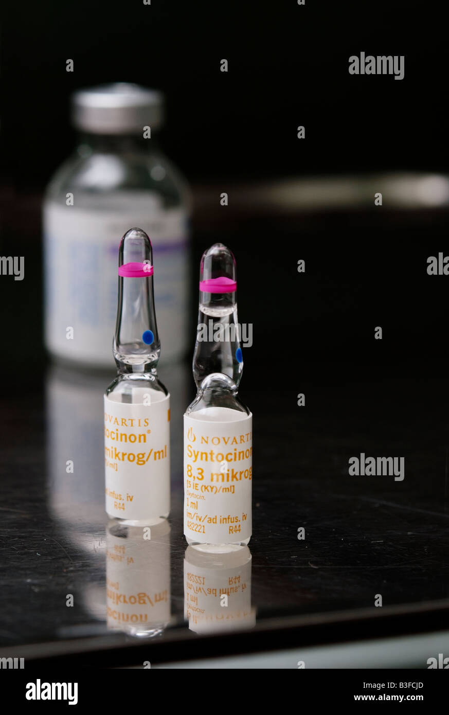 Two ampoules of Syntocinon (oxytocin) drug on steel table with a bottle of local anaesthetic in the background Stock Photo