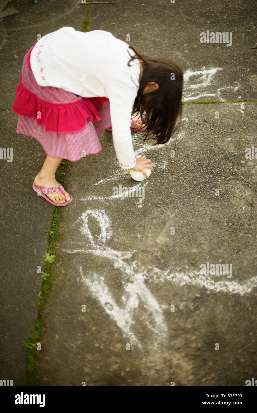 Eleanor writes her name Five year old girl uses volcanic pumice rock to draw on concrete path Stock Photo