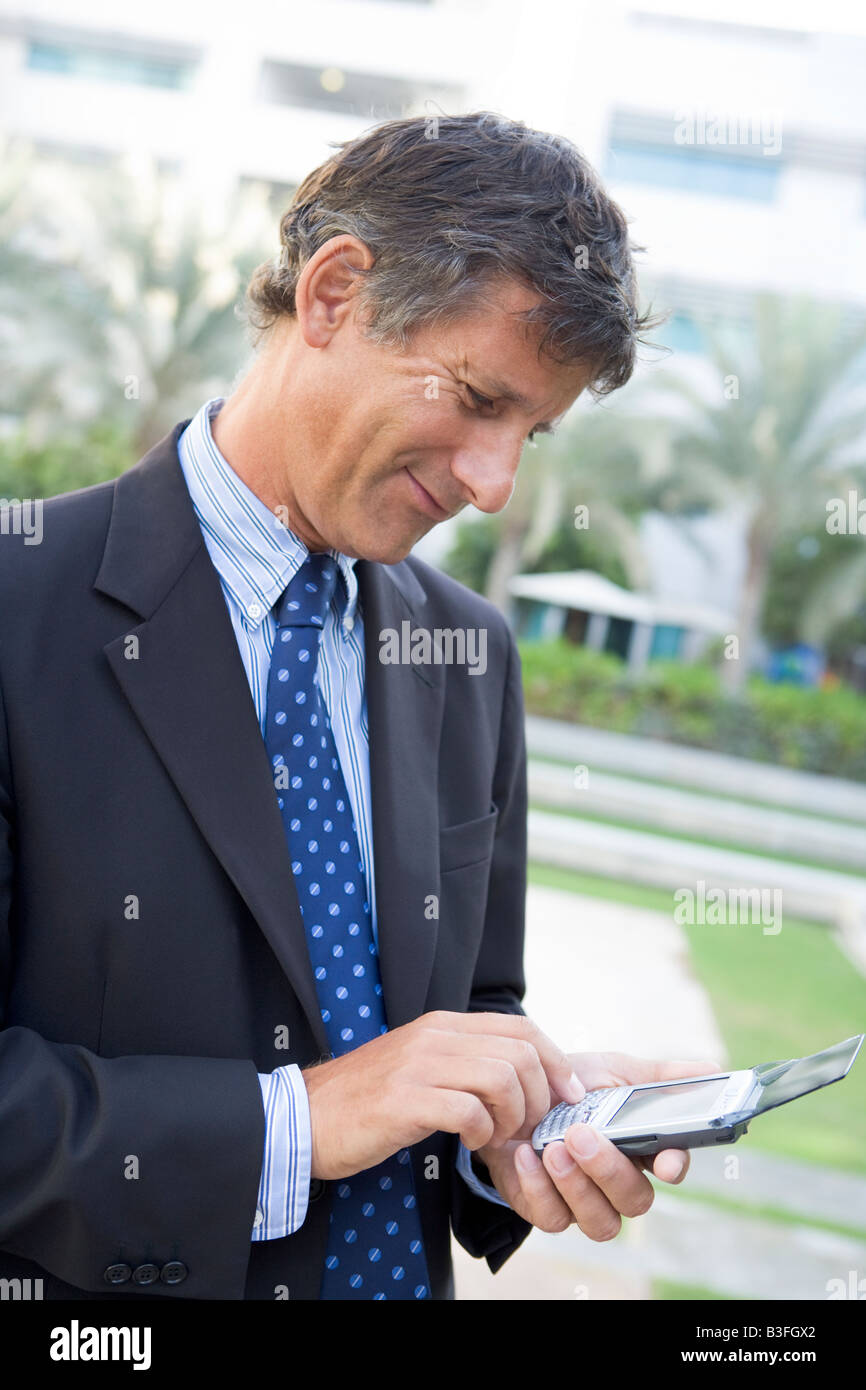 Businessman outdoors using personal digital assistant smiling Stock Photo
