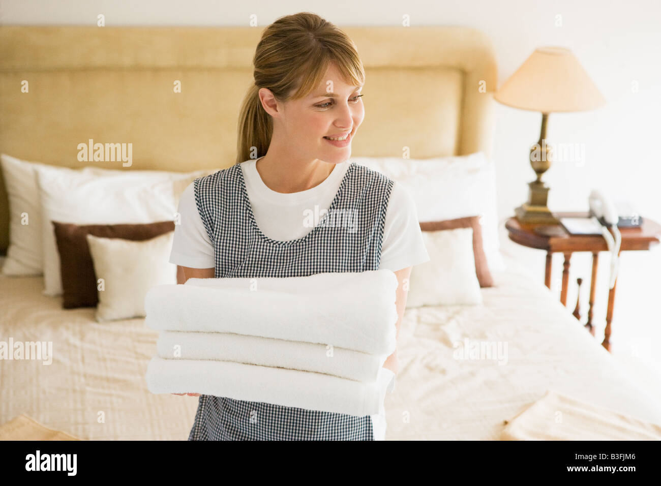 Maid holding towels in hotel room smiling Stock Photo