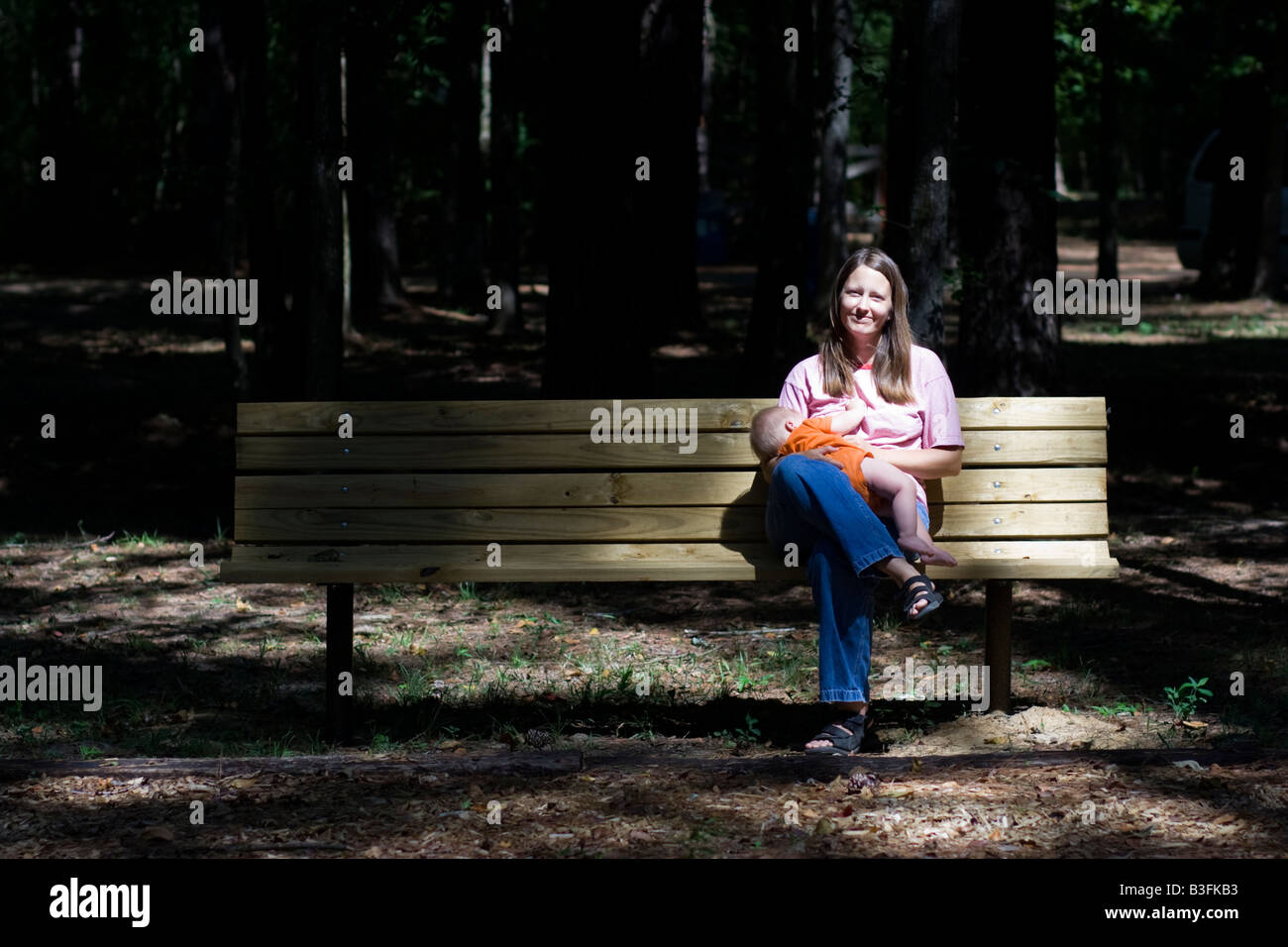 Woman on park bench nursing baby Stock Photo