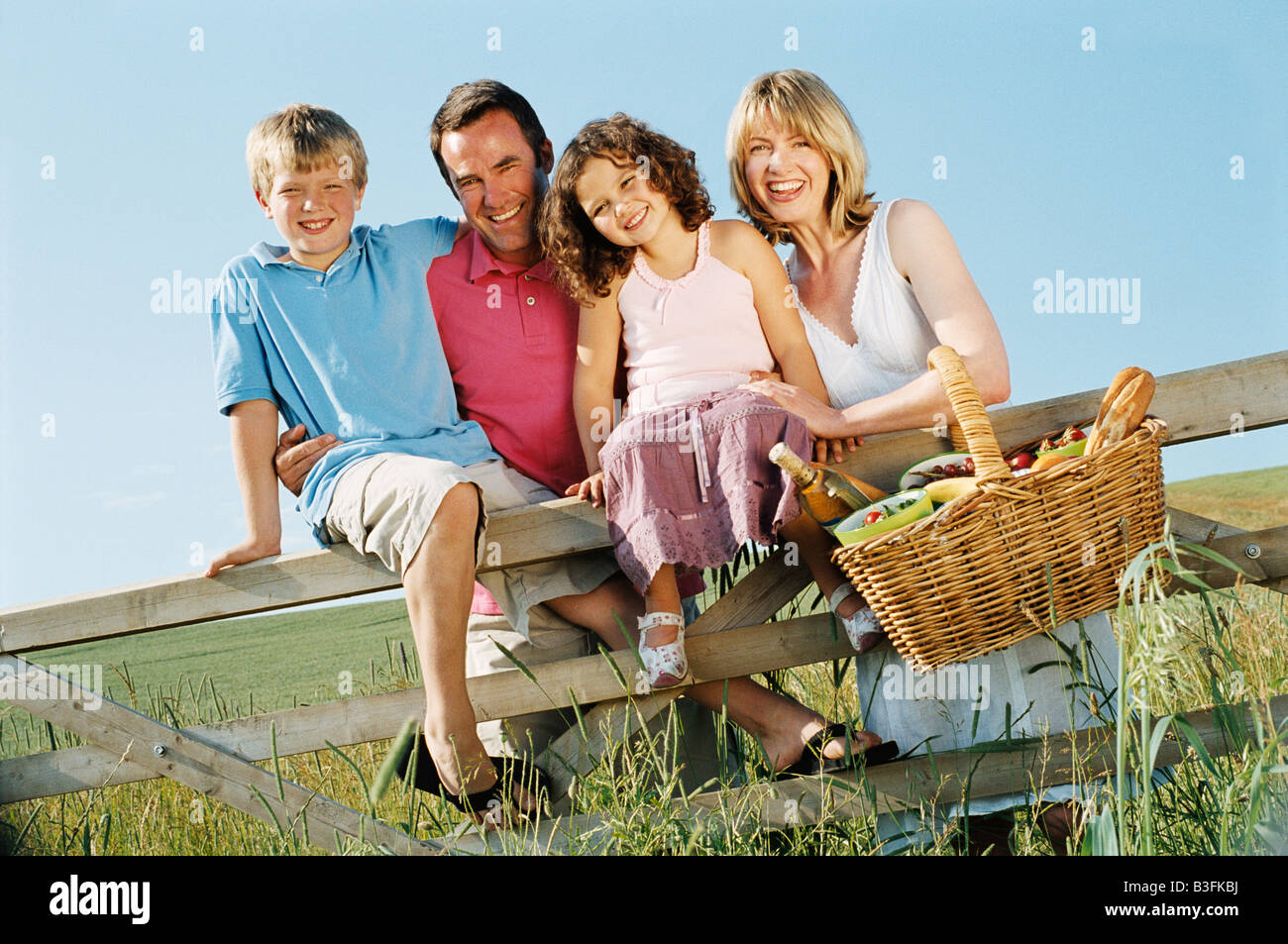 Family outdoors by fence with picnic basket smiling Stock Photo - Alamy