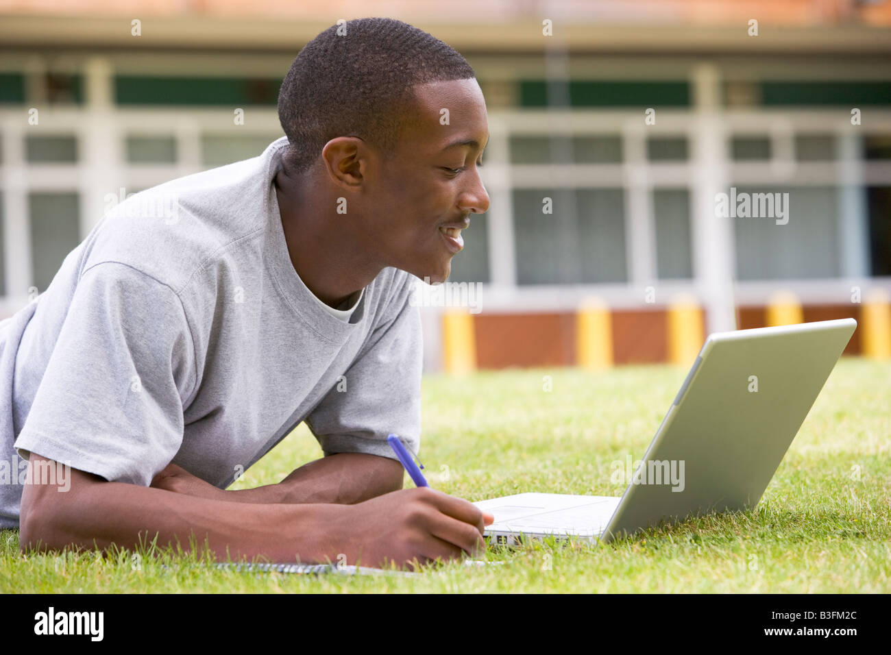 Student lying outdoors on lawn with laptop Stock Photo