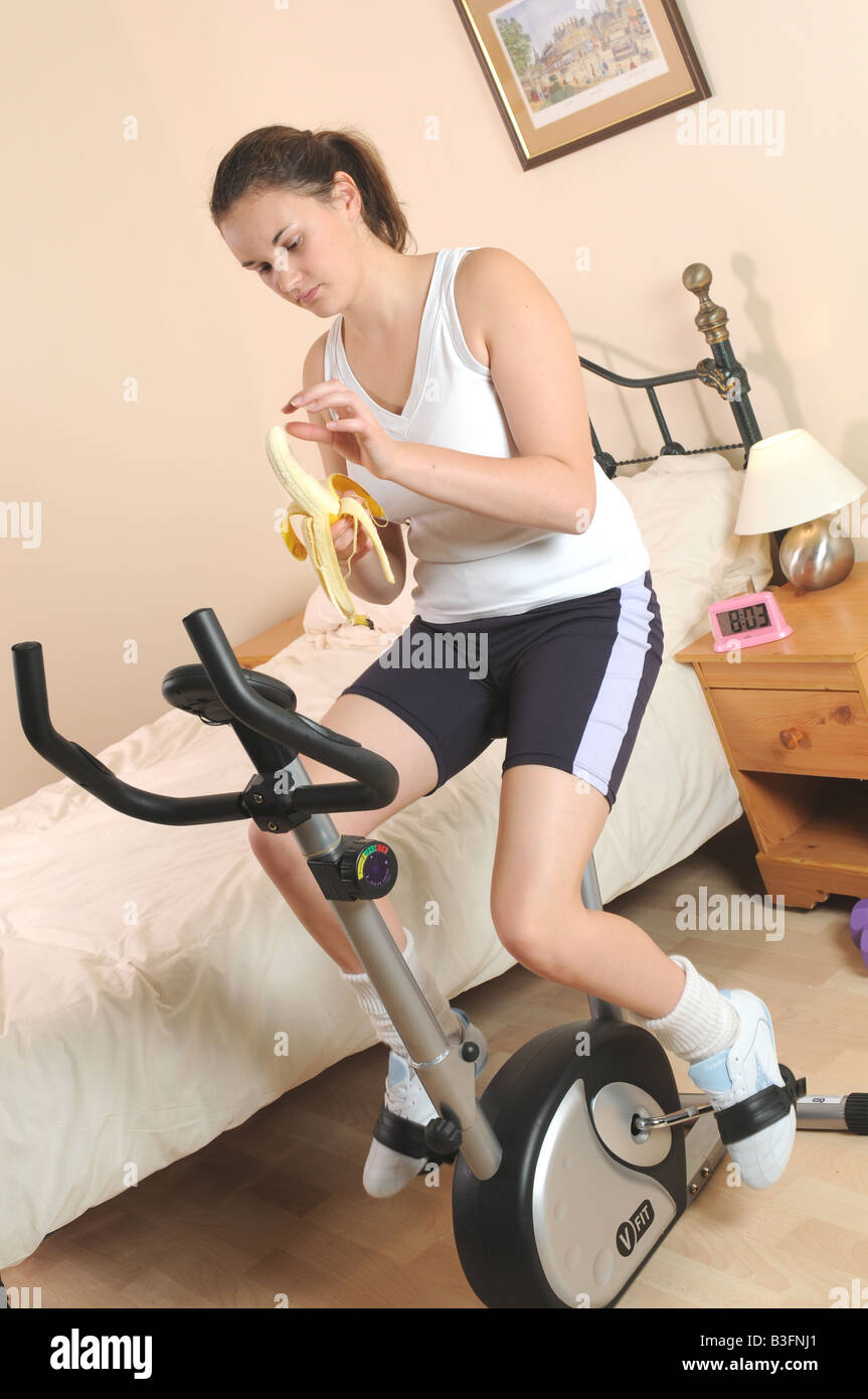 a girl fitness training on her exercise bike whilst eating an apple Stock Photo