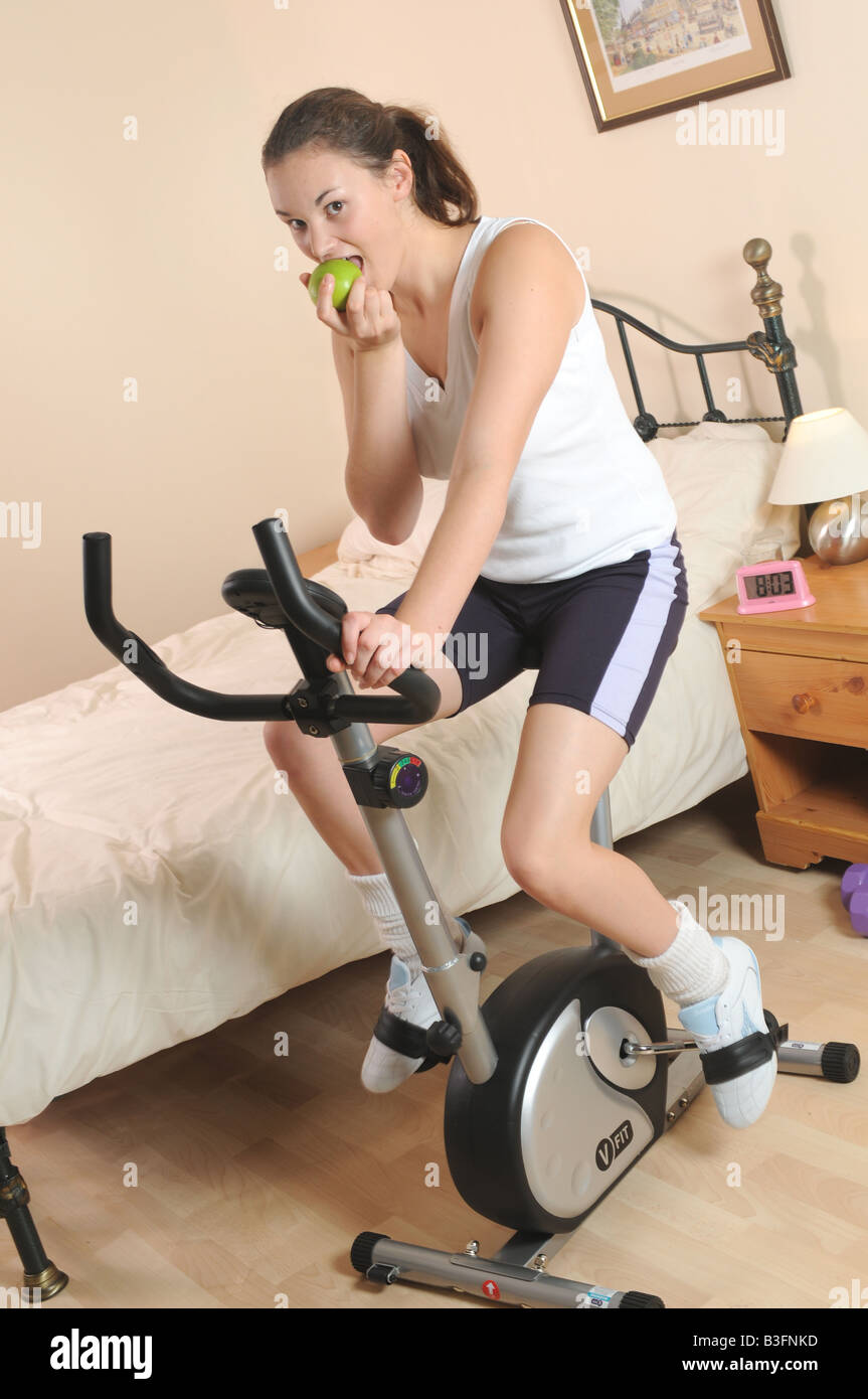 a girl fitness training on her exercise bike whilst eating an apple Stock Photo