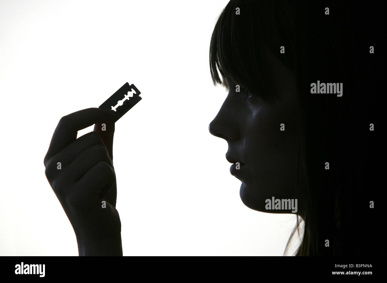 Sad young girl looking at razor blade, selfhurt, borderline syndrome Stock Photo