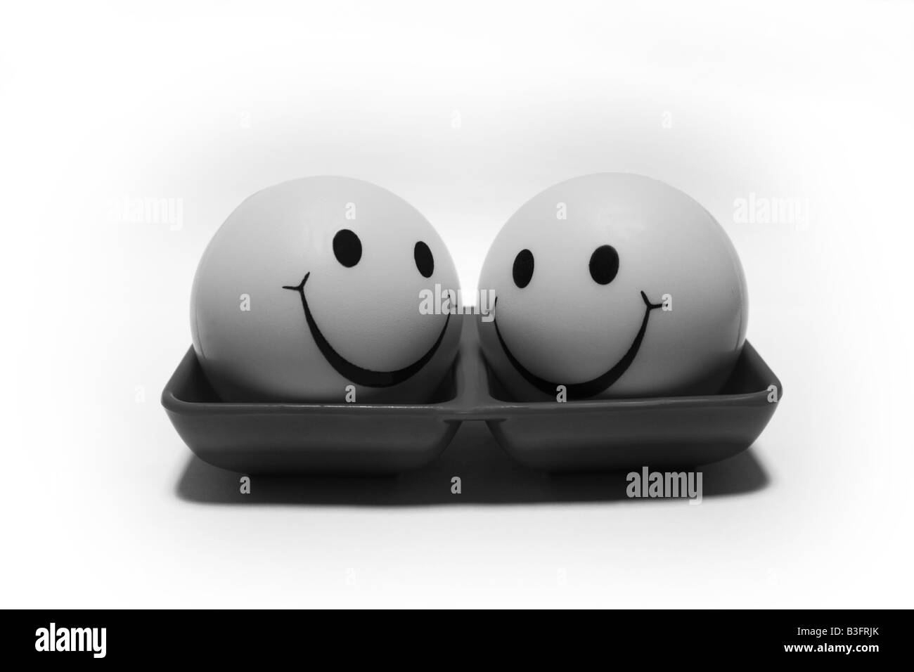 Two black and white color smiling friendly balls on a red colored double layer tray looking at each other Stock Photo