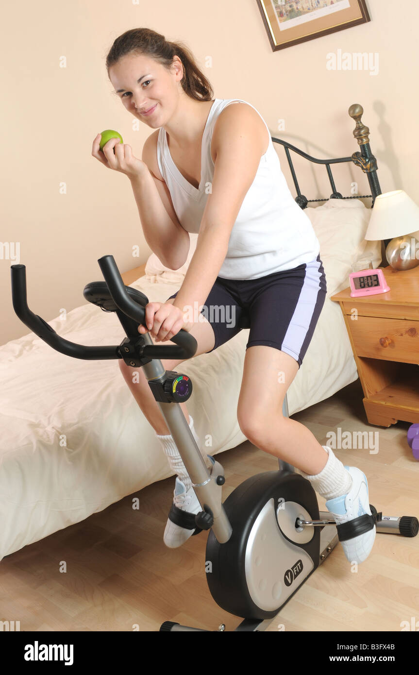 a girl fitness training on her exercise bike whilst eating an apple Stock Photo