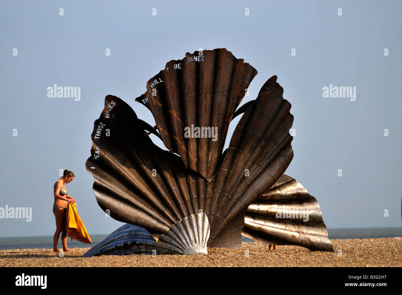sunbather prepares to lay down her towel next to scallop at aldeburgh Stock Photo