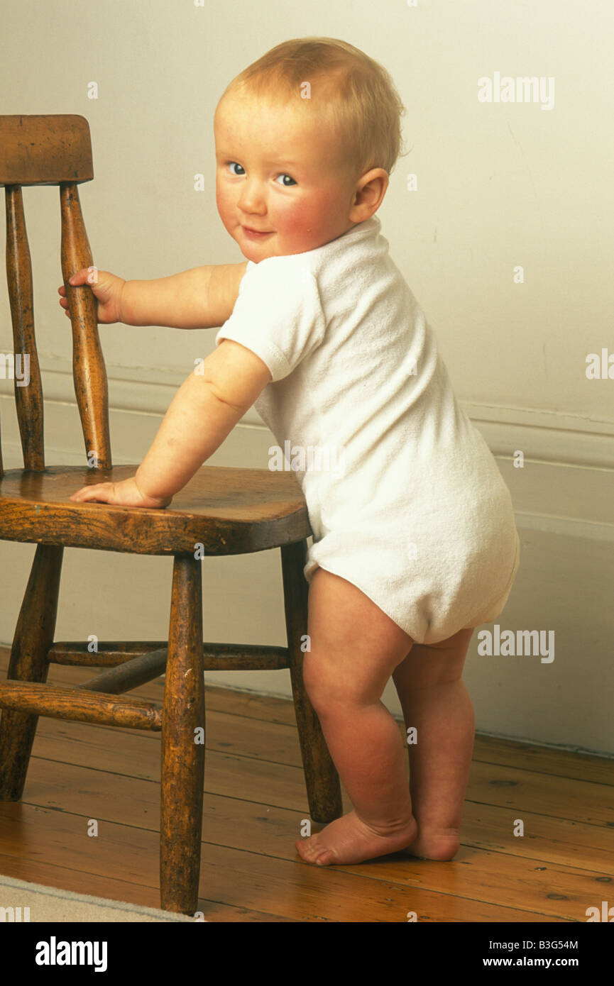 baby learning to stand pulling himself up with a small chair Stock