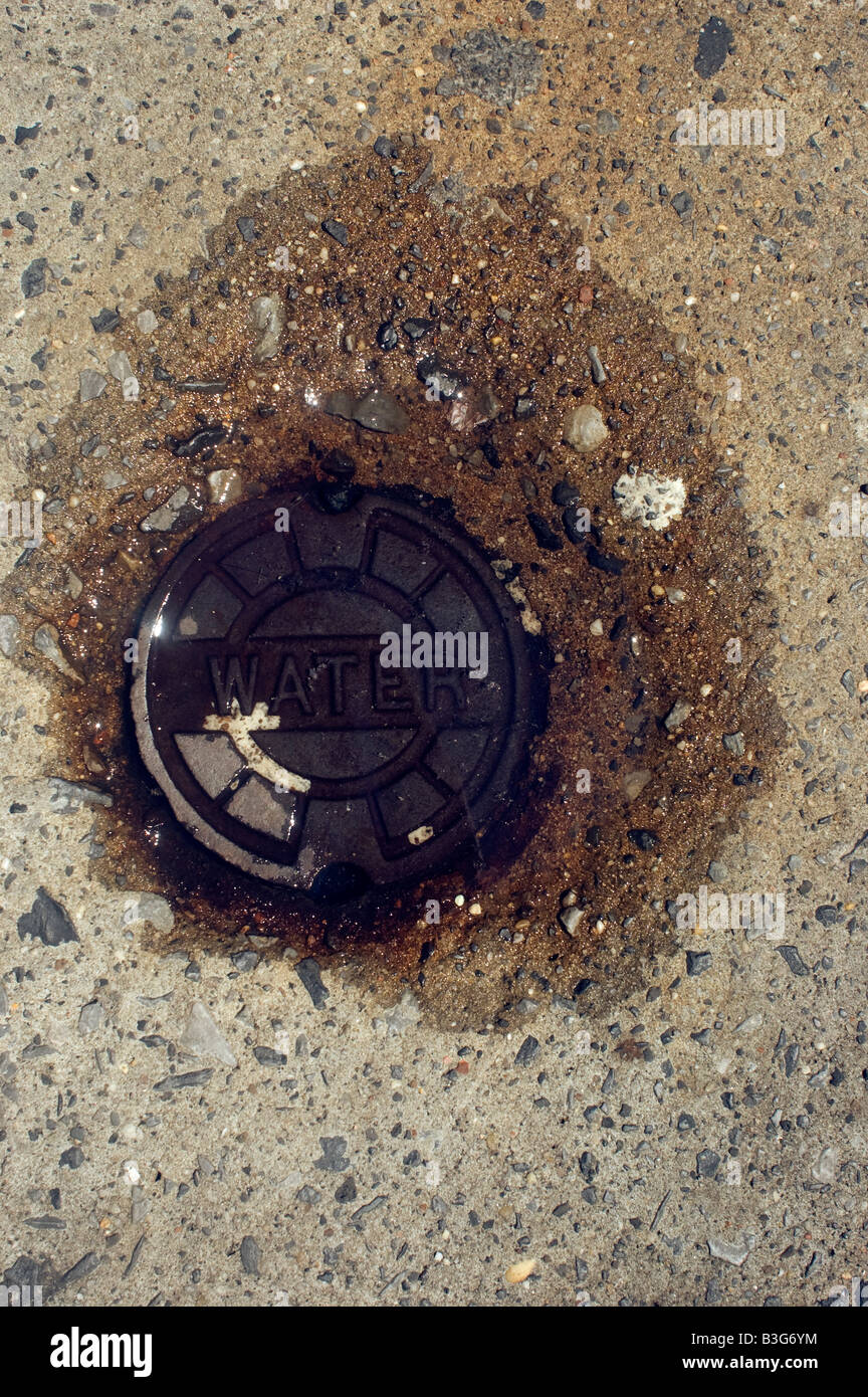 Close up of manhole cover for water main pipe in puddle of water Stock Photo