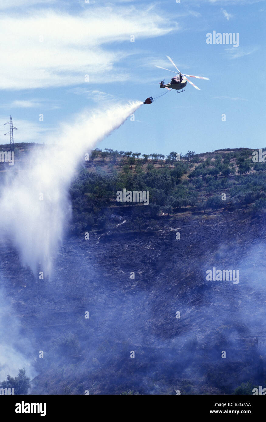 A helicopter water bombs a fire in an olive grove, Spain Stock Photo