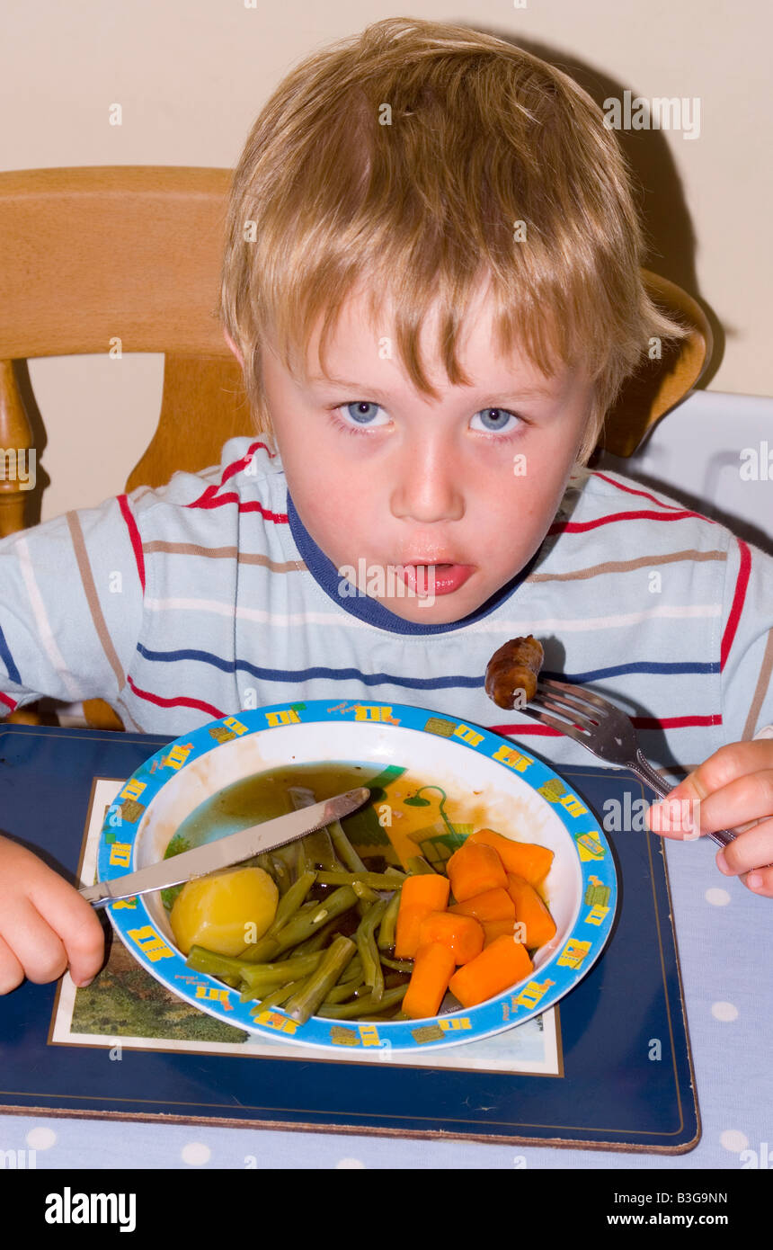 Four year old boy eating a healthy dinner with sausages  fresh vegetables and gravy. Stock Photo