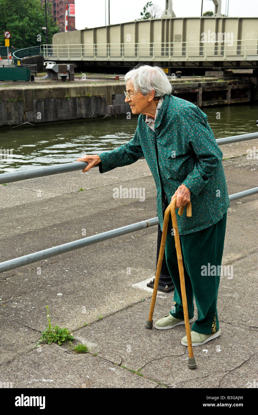 Active elderly English 92 year old woman holding two canes and holding railing while walking Bristol City docks Stock Photo