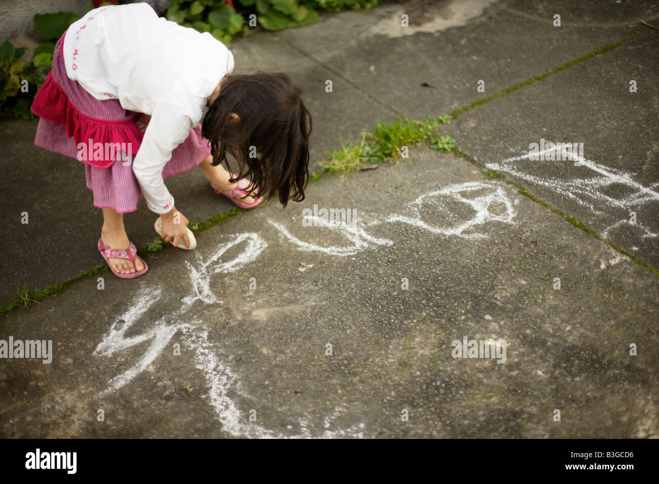 Eleanor writes her name Five year old girl uses volcanic pumice rock to draw on concrete path Stock Photo