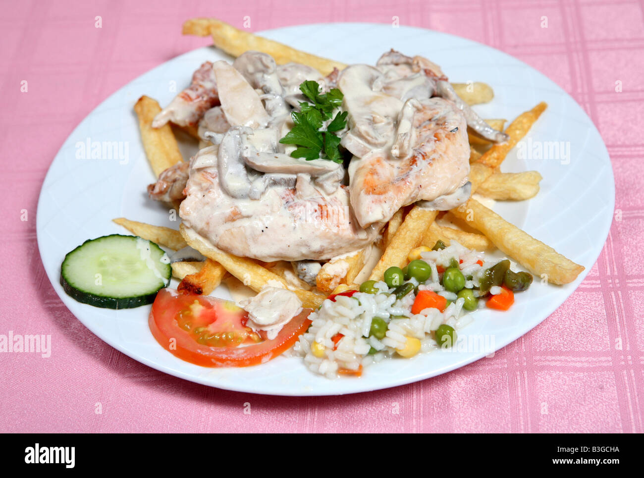 A Greek taverna meal of grilled chicken topped with mushrooms in cream and served with salad and rice Stock Photo