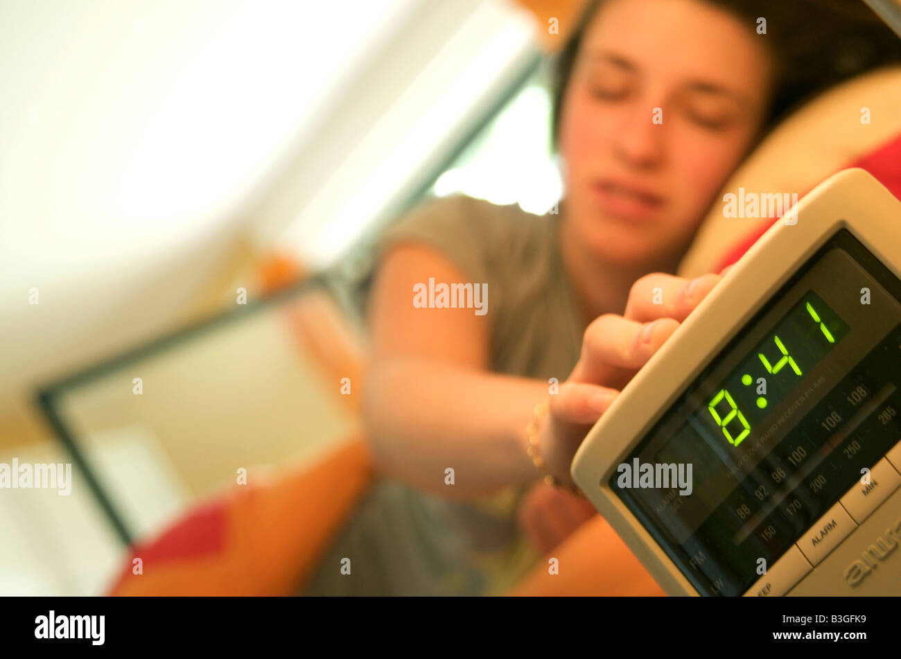 A young woman / teenager woken up in bed by her alarm clock turning it off Stock Photo