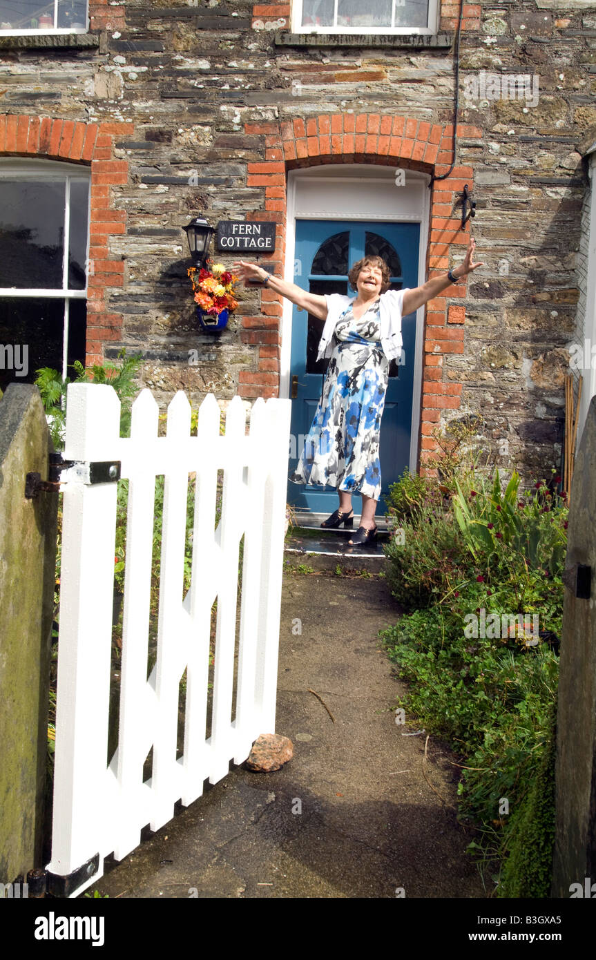 Mature lady looking happy on doorstep of her cottage home Stock Photo